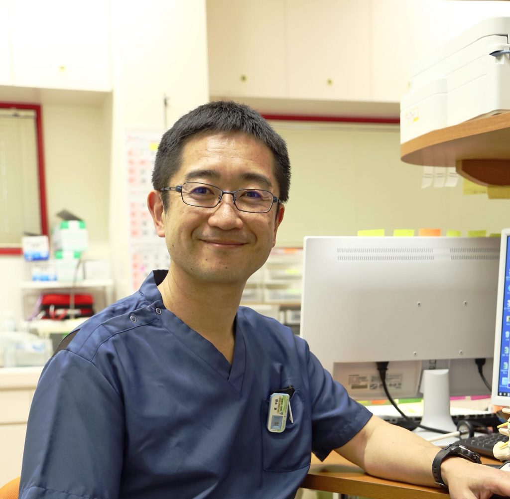 介護施設の医務室でスタッフが業務中。パソコンと医療機器が見える職場環境。